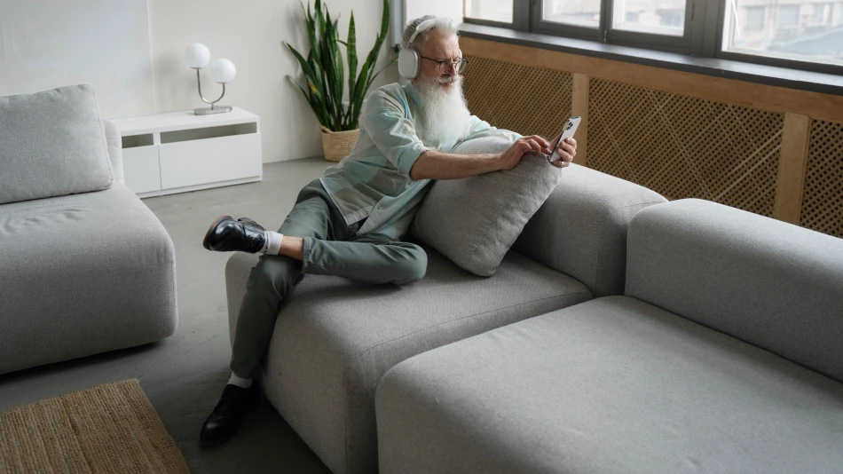 Senior man using smartphone sitting on sofa in living room