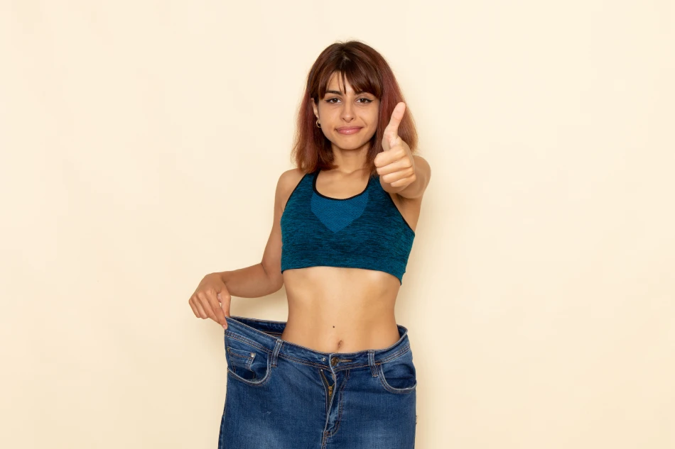 front view Young woman with beautiful body and measure tapeyoung female with fit body blue shirt jeans smiling light white wall